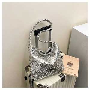 Detail of silver sequined handbag with twisted rope shoulder strap hanging on a suitcase