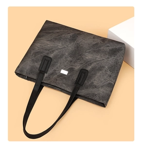Detailed view of large dark grey canvas tote bag with black leather straps and logo plaque