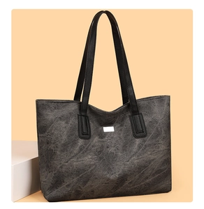 Front detail of large dark gray tote bag with dual shoulder straps and metallic plate