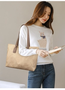 Close-up of light brown textured leather tote bag with dark handles held by a model