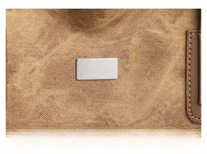 Detailed close-up of brown canvas texture with leather trim and metal plate on tote bag