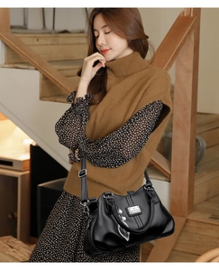 Detail of black pebbled leather handbag featuring metal leaf charm and pearl accessory