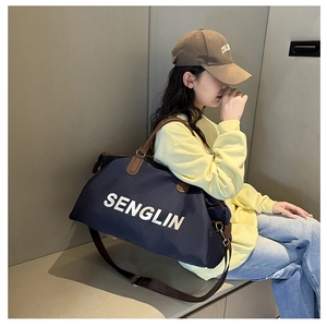 Detail of navy travel bag with brown straps and white logo worn by a female model