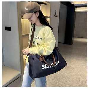 Detail of navy blue large travel bag with brown handles carried by a model in a modern hallway