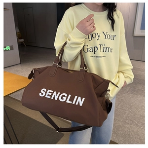Detail of chocolate brown travel duffel bag with white letters and adjustable shoulder strap