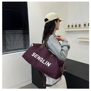 Detail view of large purple travel duffel bag with brown leather handles and shoulder strap