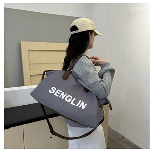 Detail of gray travel bag with white lettering and sturdy brown leather handles