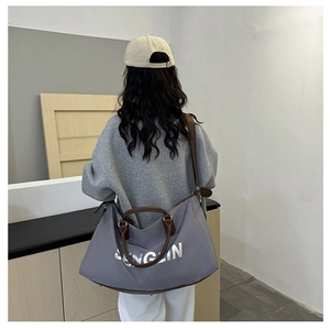 Rear view of a large grey nylon travel bag with brown leather handles on a female model