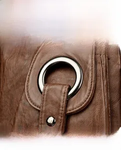 Detail view of dark brown pebbled leather texture with silver metal ring buckle and rivet