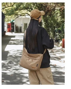 Detail of khaki canvas crossbody bag featuring adjustable strap and leather logo patch