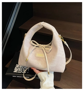 Detail of minimalist beige handbag with drawstring bow and gold hardware on stairs