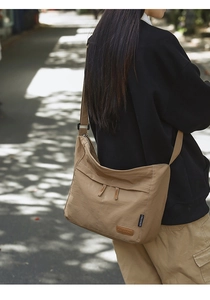 Detailed side view of khaki crossbody bag showing front zipper pockets and brand label