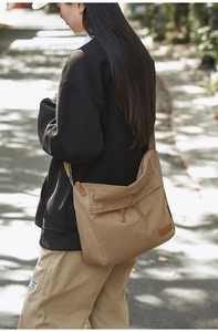 Detailed back view of a large khaki nylon messenger bag worn on shoulder in street style