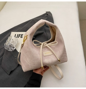 Detail of pink corduroy shoulder bag with HAMIRCO plaque and bow on gray blazer background