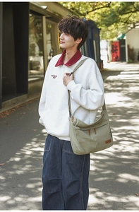Detail of olive green canvas messenger bag worn with casual streetwear outfit outdoors