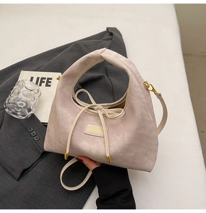 Close-up of pink textured hobo bag with gold hardware on a grey blazer and magazine