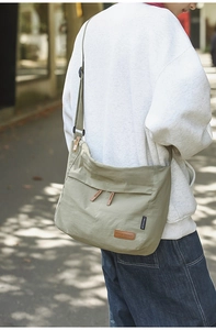 Detail of olive green messenger bag featuring dual front zipper pockets and leather pulls