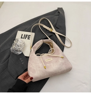Detail of light purple suede handbag with gold hardware and knot accent on a grey blazer
