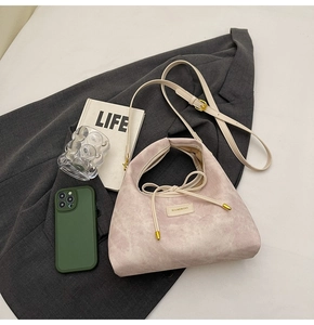 Detail of lavender suede bag with drawstring bow and brand tag on grey suit