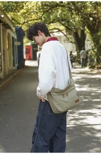 Close-up of olive green crossbody bag with leather puller in outdoor sunlight