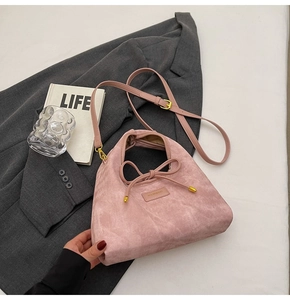 Detail of pink suede handbag with decorative bow drawstring and gold metal logo accent