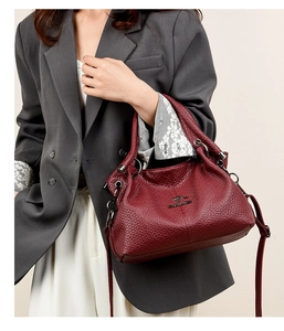 Detail of dark red lychee textured leather tote bag featuring golden kangaroo metal logo