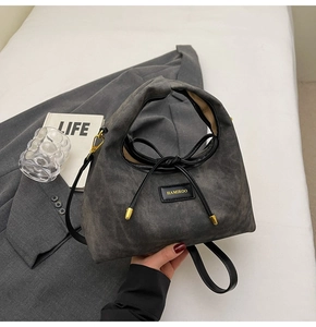 Close-up of gray twill handbag with knotted handle, black bow, and gold metal hardware