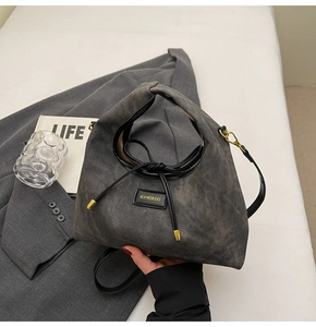 Close-up of grey washed denim handbag with black leather brand plaque and gold hardware