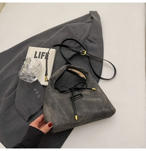 Detailed view of dark grey suede crossbody bag with black bow and adjustable gold hardware