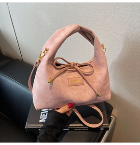 Detail of pink suede handbag with decorative bow drawstring and golden metal hardware