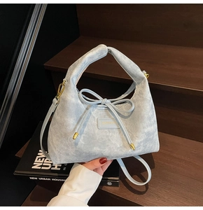 Close-up of light blue textured handbag with bow drawstring detail and golden hardware