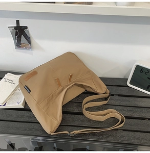 Detail of khaki minimalist canvas messenger bag with brand tag on wooden bench