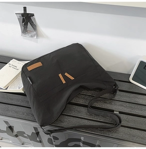 Detail of black nylon shoulder bag showing brown leather patch and side brand label