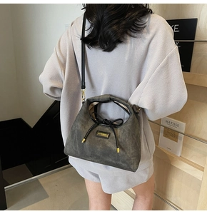 Detail of grey crossbody bag with HAMIROO gold logo and knotted cord on high-end suede texture