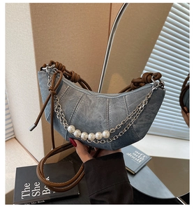Dettaglio borsa a mezzaluna in denim con catena di perle e tracolla in pelle marrone