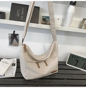 Detail of cream nylon crossbody bag featuring wide strap and premium brown leather logo tag