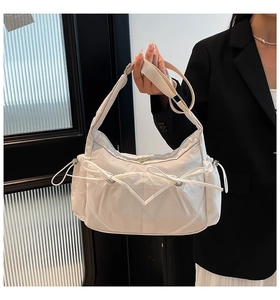 Gros plan d'un sac à bandoulière crème avec nœuds décoratifs et cordons de serrage