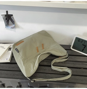 Close-up of light green large capacity canvas crossbody bag with wide strap and logo detail