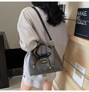 Detail of grey suede shoulder bag featuring decorative bow and golden hardware