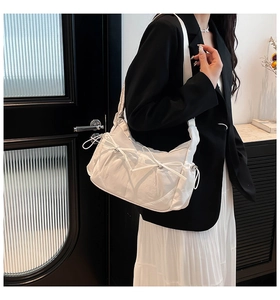 Sac bandoulière blanc plissé avec nœud coulissant porté par un mannequin en décor intérieur