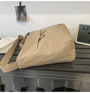Detail of a large khaki nylon crossbody bag with adjustable wide strap on a bench