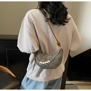 Detail of grey canvas crescent bag with silver chain and decorative pearl strap