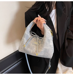 Detail of grey-blue handbag with bow drawstring and gold logo tag worn on black blazer