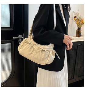 Sac bandoulière plissé blanc crème avec nœud coulissant porté par un mannequin élégant