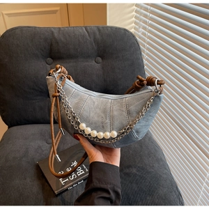 Detail of blue denim crescent bag with faux pearl chain and brown leather knot handle