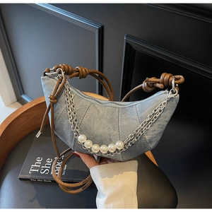 Detail of light blue denim croissant bag with silver chain and pearl decorations