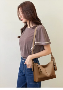 Close-up of brown lychee grain leather crossbody bag with side drawstring detail on model