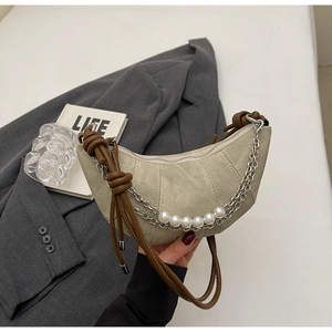 Detail of beige crescent bag featuring silver chains, pearls and brown leather strap