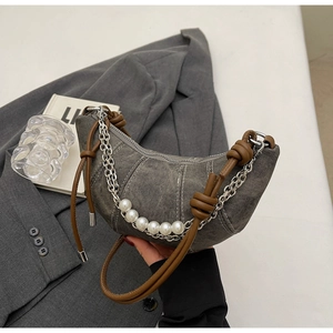 Detail of grey crescent bag featuring silver chains and large white pearls on grey blazer
