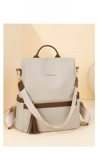 Close-up of beige nylon backpack with brown leather trim and golden metal logo plate